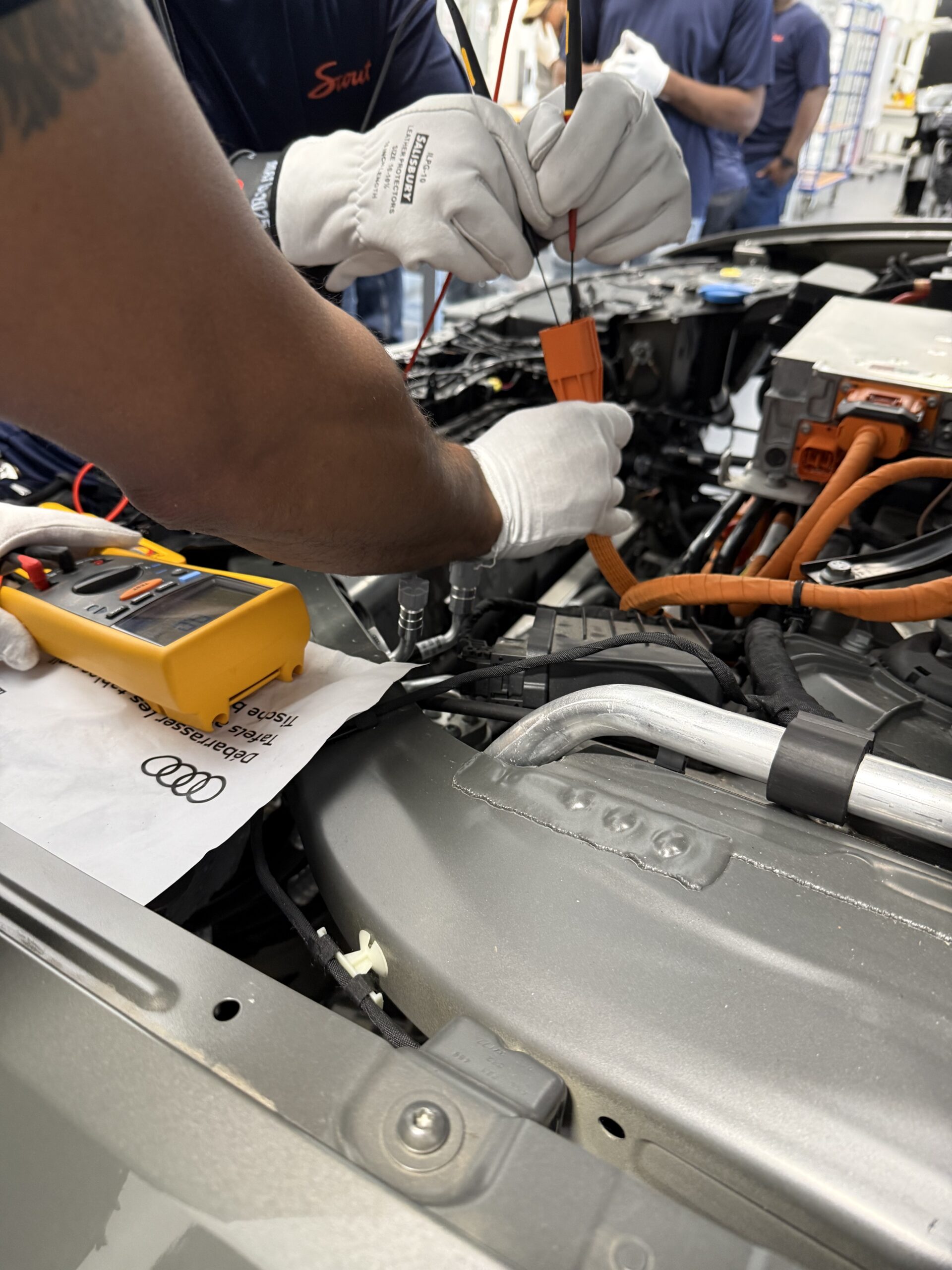 Gloved hands testing an EV high voltage connector during ElecTrain training