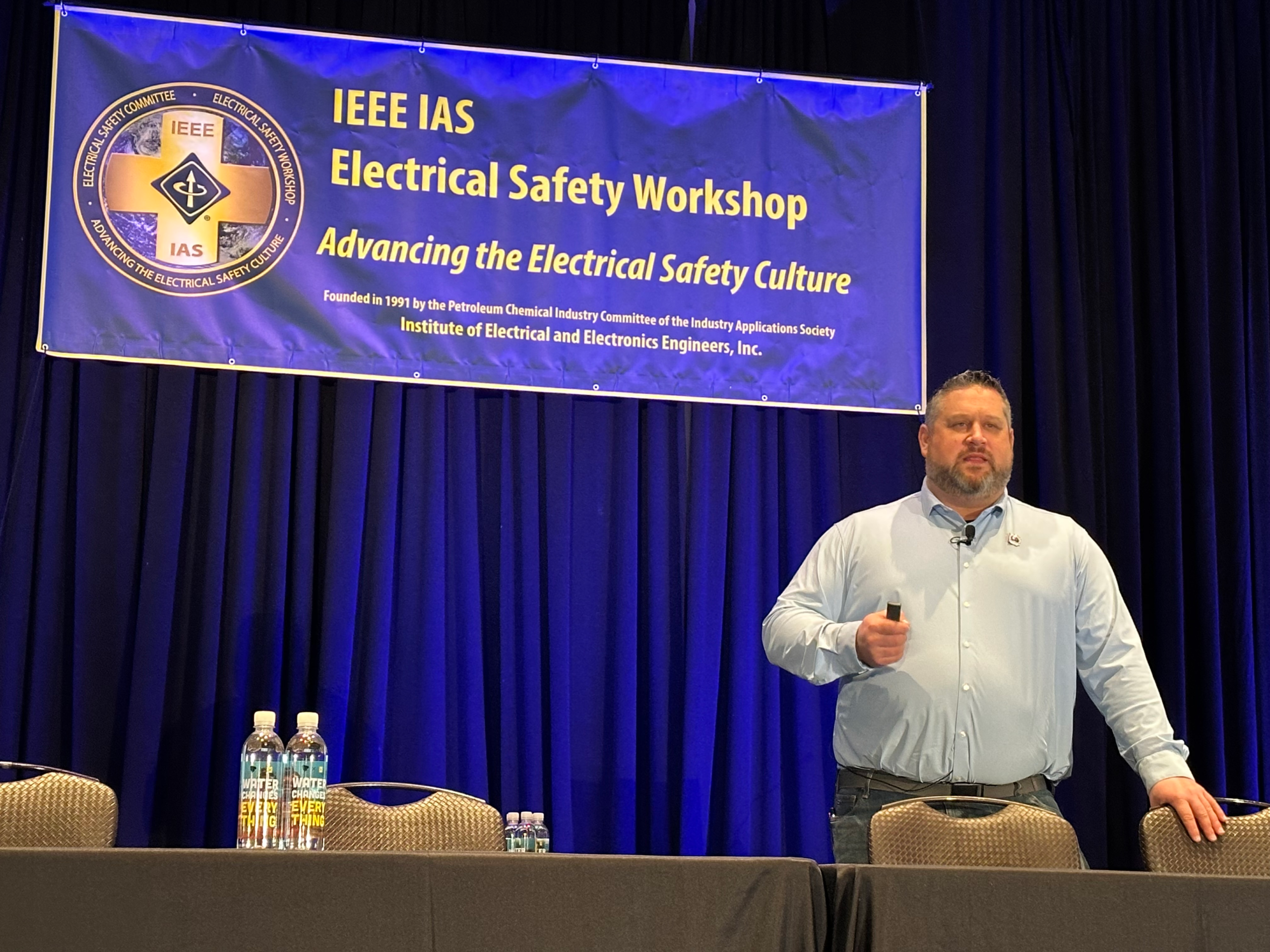 Presenter holding a presentation remote beneath the IEEE IAS Electrical Safety Workshop banner.